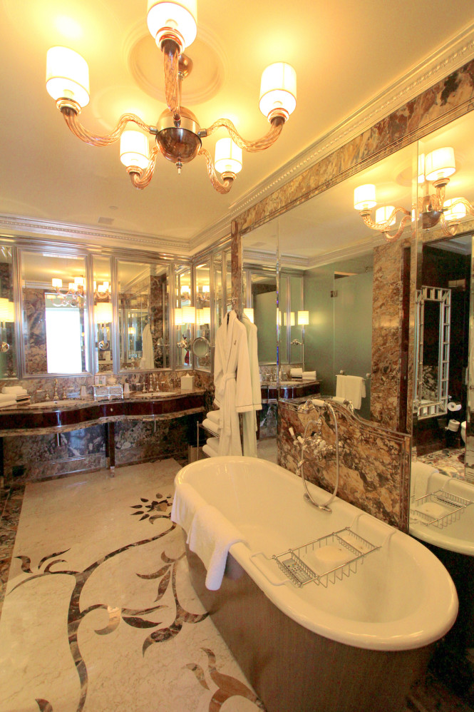 The opulent bathroom has a tub that sits right opposite a television screen.