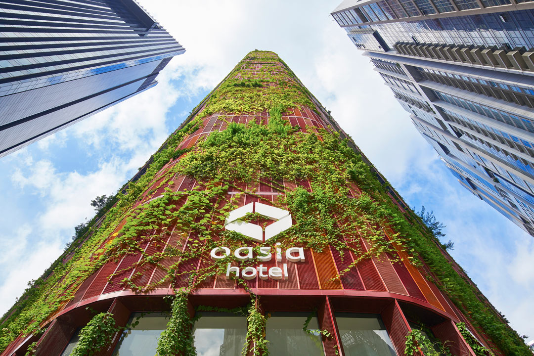 Red aluminum mesh and leafy foliage envelope Oasia Hotel Dowtown's facade.