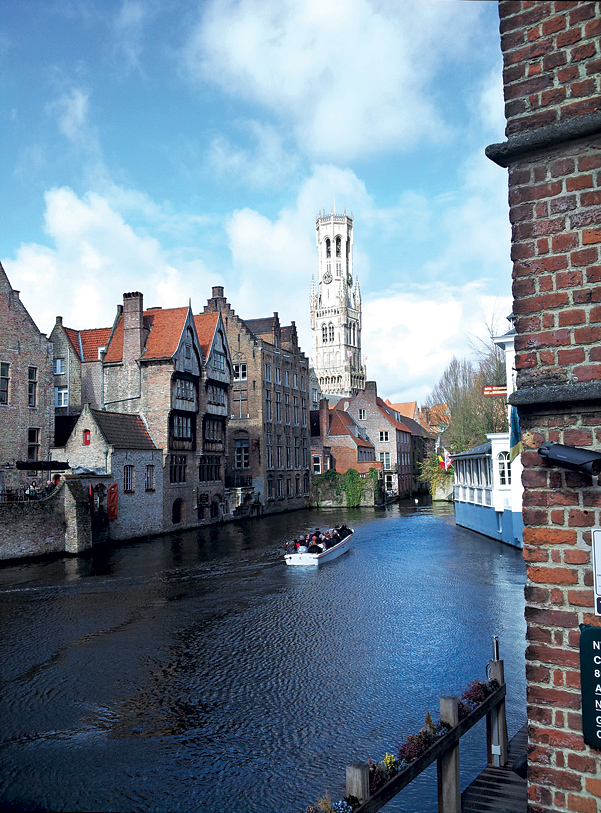 A canal boat at Rozenhoed Quay in Bruges, with the city's medieval bell tower as a backdrop.
